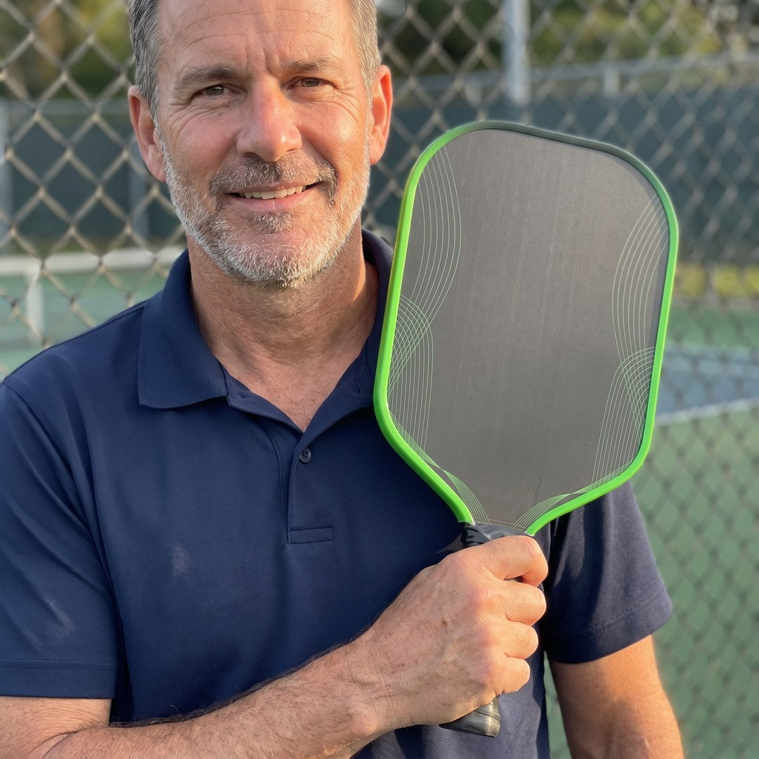Man courtside holding the green-edge Dinkwell 16 mm honeycomb carbon pickleball paddle