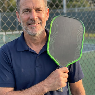 Man courtside holding the green-edge Dinkwell 16 mm honeycomb carbon pickleball paddle