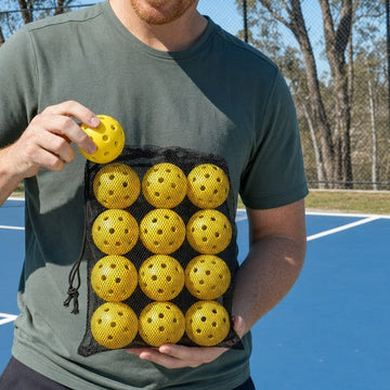 Hand taking a yellow pickleball from the mesh bag of twelve