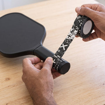 Hands starting an overgrip at the butt end of a paddle handle
