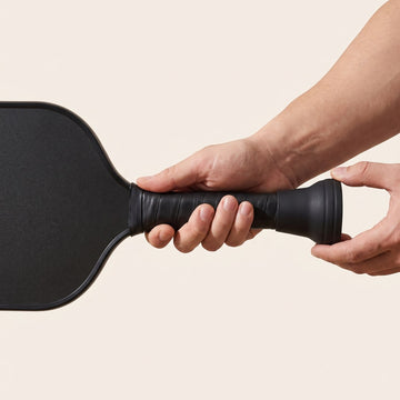 Hands sliding the rubber ball picker onto the butt end of a paddle handle