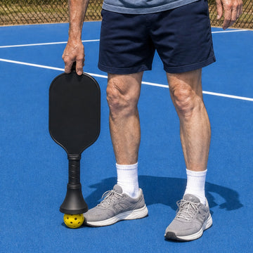 Paddle held upside down, pressing the ball picker onto a pickleball on the court