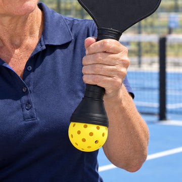 Yellow pickleball held in the ball picker cup on the end of a paddle handle